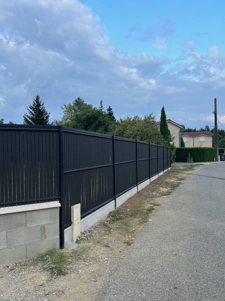 Clôture occultante posée sur un muret le long d’un chemin